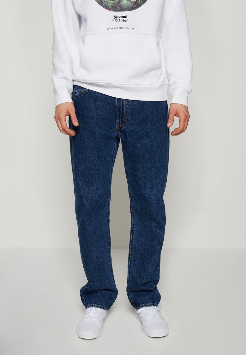 Slim-fit mörkblå jeans med urblekt textur, femfickorsdesign och bältesöglor. Bärs med en vit hoodie och vita sneakers.