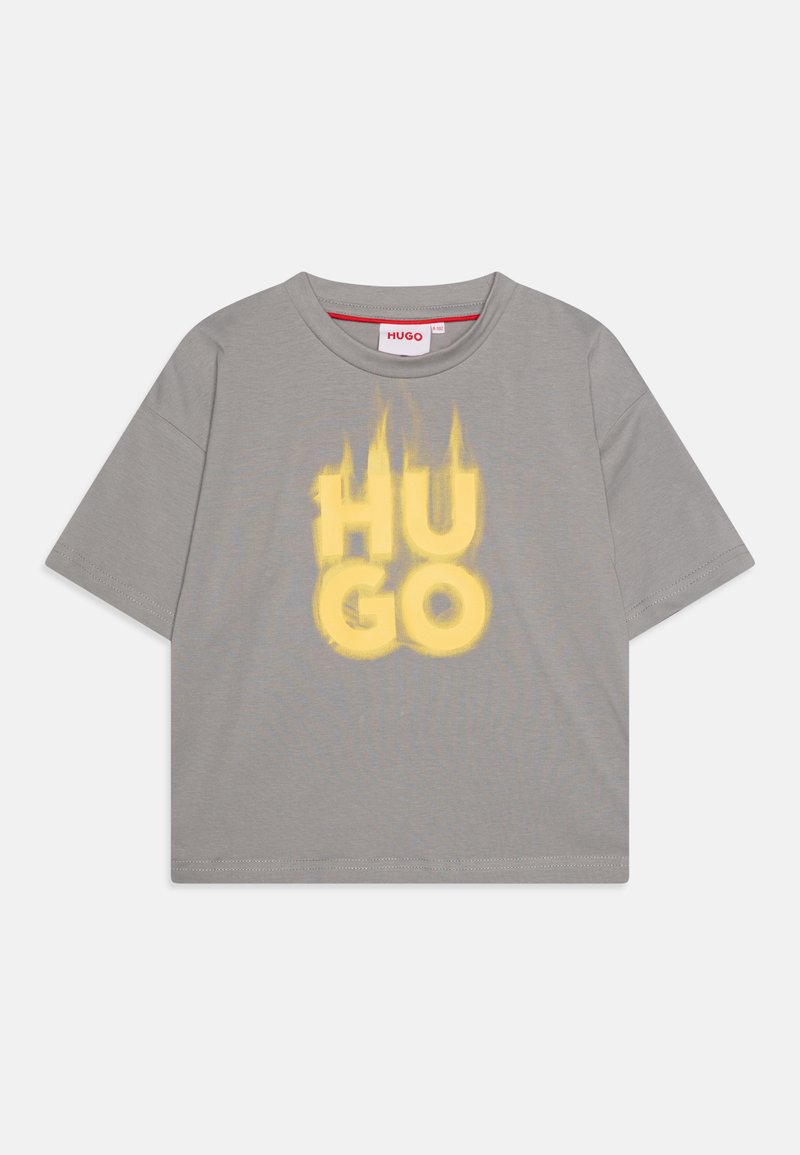 T-shirt cinza de manga curta com uma grande impressão gráfica em amarelo do texto "HU GO" em estilo desgastado. Material de algodão com gola redonda.