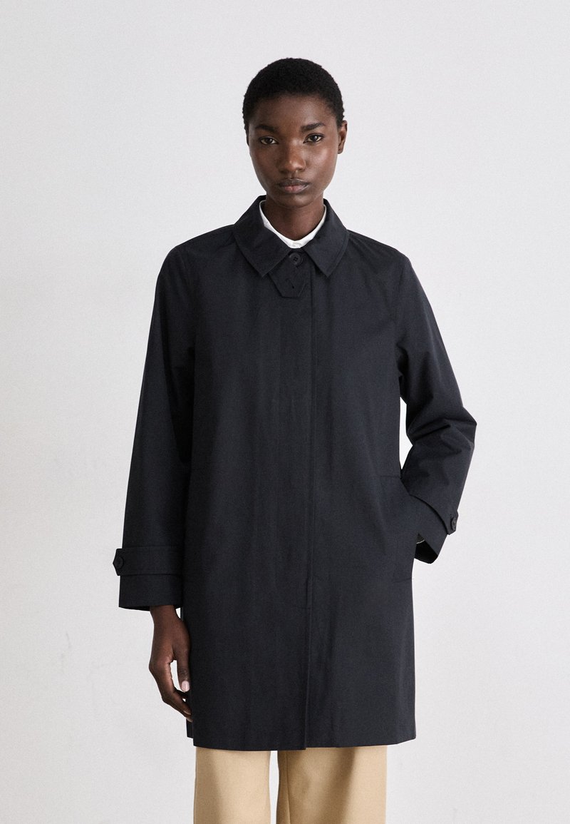 Abrigo negro impermeable con un diseño limpio, que presenta un cuello puntiagudo, mangas largas y bolsillos laterales. Textura suave, con un detalle mínimo.