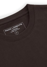 Ciemnobrązowy, oversize'owy t-shirt z czystej bawełny, z okrągłym dekoltem i widoczną wewnętrzną metką z nazwą marki oraz rozmiarem medium.
