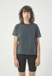 Dunkelgraues Baumwoll-T-Shirt mit Rundhalsausschnitt und kurzen Ärmeln, kombiniert mit schwarzen Radfahrer-Shorts. Glatte Textur, lockere Passform, minimalistisches Design.
