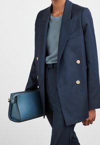 Námořnický dvojřadý blazer se zlatými knoflíky, světle modré tričko, odpovídající kalhoty a strukturovaná modrá kabelka se zipovým uzávěrem.