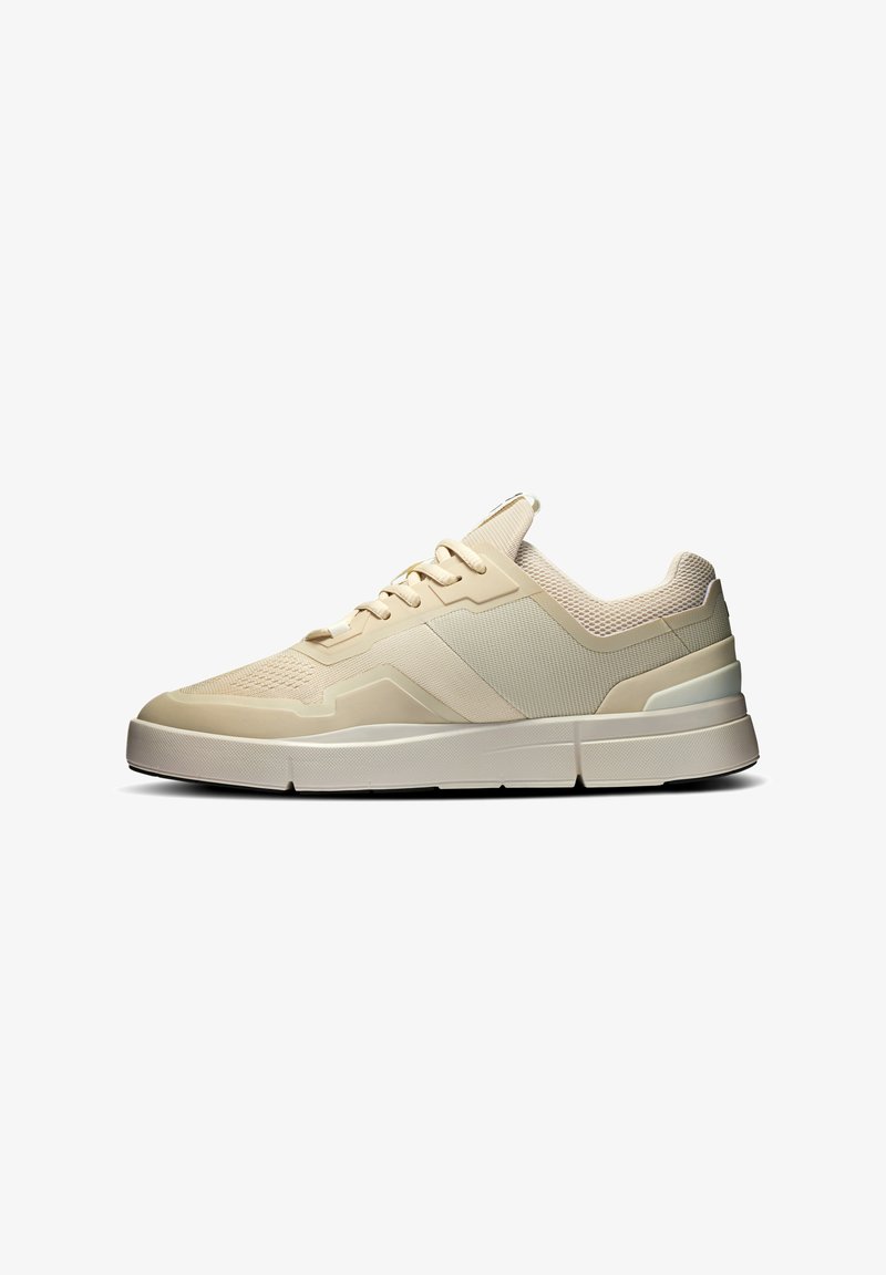 Beige atletiska skor med en strukturerad mesh-överdel, vadderad krage och kontrasterande gummisula. Har en strömlinjeformad design och klassisk snörning.