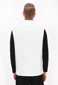 Weißer Fleece-Weste mit hohem Kragen, schwarzen langen Ärmeln und glatter Textur. Einfaches Design, geeignet für das Tragen in kühlerem Wetter.
