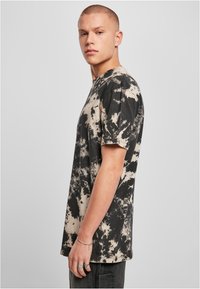 Svart og beige tie-dye bomull t-skjorte med korte ermer, rund hals og løs passform; har et sprutet design over hele.