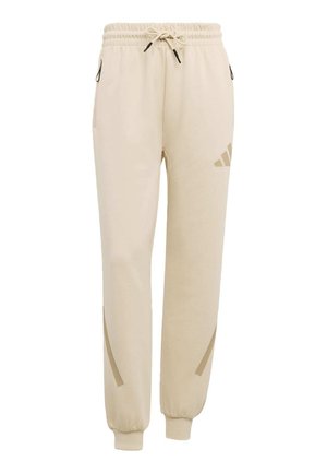 Pantalones deportivos beige con cintura elástica, cordón ajustable, puños en los tobillos, bolsillos laterales con cremallera y logo sutil en el muslo superior y la parte inferior de la pierna.