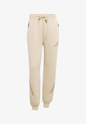 Beige sweatpants with elastic waistband, drawstring, ankle cuffs, zippered side pockets, and subtle logo on upper thigh and lower leg.