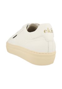 White leather sneaker with a textured surface, beige rubber sole, and a black accent. "ekn" logo in gold on the heel. Classic lace-up design.