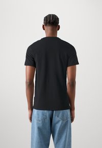 Sort bomulds t-shirt med korteærmer og rund halsudskæring, vist fra ryggen. Matchet med lyseblå denimbukser.