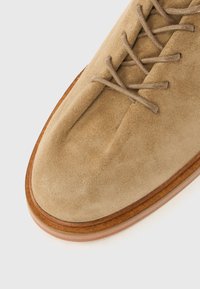Chaussure en daim marron clair avec un bout rond, des lacets fins assortis et une semelle beige lisse. Présente un design épuré et simple.