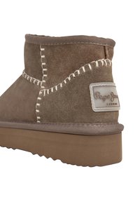 Barna nubuk bokacsizma vastag talppal, fehér varrásokkal, és "Pepe Jeans London" címkével a sarkán.