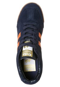 Sneaker in suede blu navy con strisce arancioni, lacci rotondi e suola in gomma. Presenta un logo dorato su una soletta bianca. Design atletico classico.