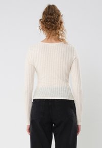 Aansluitend lange mouwen top in lichtbeige ribstof met een ronde halslijn. De achterkant heeft een geleidelijke kleurovergang naar een lichtere tint.