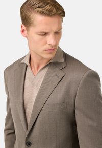 Blazer grigio texturizzato con rever a battente e chiusura a un bottone, indossato sopra un maglione beige chiaro a scollo a V.