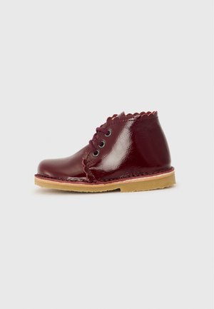 Botte en cuir verni bordeaux avec col festonné, design à lacets et semelle en caoutchouc beige. Texture lisse et finition brillante.