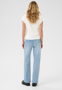 Witte korte mouw top gecombineerd met lichtblauwe wijde jeans, met subtiele steken en een rechte snit, afgemaakt met zwarte plateau schoenen.