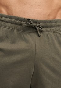 Gros plan sur la taille d'une personne portant un pantalon à taille élastique vert olive avec un cordon noué et la peau visible du bas du dos.