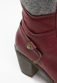 Burgundzkie skórzane botki z filcową cholewą, posiadają dekoracyjną brązową taśmę oraz mosiężny zatrzask. Słupkowy obcas z textured powierzchnią.