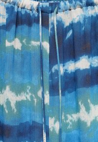 Țesătură albastră tie-dye cu nuanțe variate, având o textură pliată și un brâu elastic cu șnururi pentru ajustare.