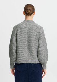 Gray knitted sweater with a textured finish, ribbed cuffs, and a boxy fit, worn over a navy skirt, showing back detail and silhouette.