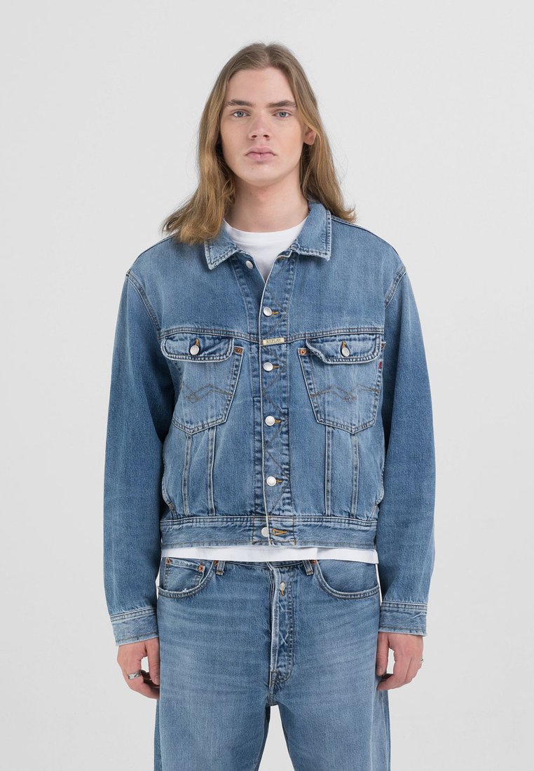 Blå denimjakke med klassisk snitt, har knappelukking, brystlommer og subtil falming. Kombinert med matchende blå denimjeans.