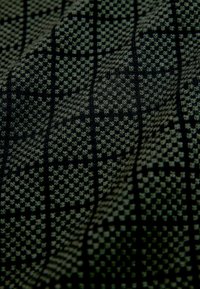 Gros plan sur un tissu foncé avec un petit motif à carreaux noirs et gris, montrant la texture et les plis.