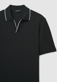Schwarzes Poloshirt aus strukturiertem Stoff mit V-Ausschnitt und kontrastierendem weißen Besatz entlang von Kragen und Ärmeln. Etikett sichtbar innen am Kragen.