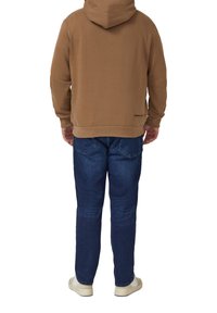 Brązowa bluza z kapturem, przednią kieszenią i ściągaczem na dole. Nosi się ją z niebieskimi dżinsami i białymi trampkami. Widoczne logo marki na dolnej części pleców.
