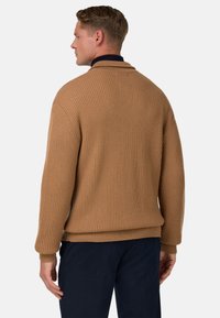 Bruine gebreide trui met ribbelstructuur, een sjaalkraag en verlaagde schouders. Heeft een comfortabele pasvorm en lange mouwen.