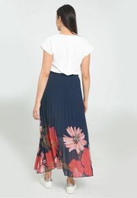 Fållad marinblå kjol med rosa blommönster, kombinerad med en kortärmad vit topp. Kjolen har resårlinning och är knälång.