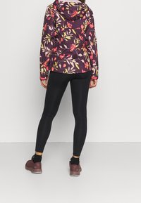 Fialová bunda vzoru květin s kapucí, v kombinaci s černými legínami a vínovými botami. Bunda má živé, detailní květinové akcenty.