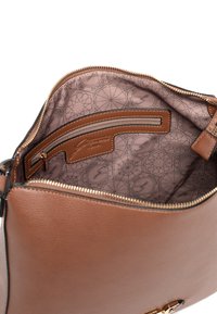 Interno di borsa in pelle marrone con tasca con zip, fodera a motivi rosa chiaro con disegni geometrici e etichetta brandizzata color cuoio.
