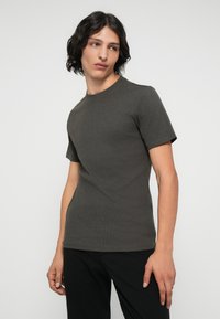 T-shirt corto grigio scuro a maniche corte, scollatura rotonda, texture a coste, design aderente, abbinato a pantaloni neri. Tessuto liscio senza fantasie.