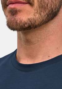 Granatowy bawełniany t-shirt z okrągłym dekoltem; widoczne szwy wzdłuż kołnierza oraz zbliżenie na zarost i strukturę skóry.