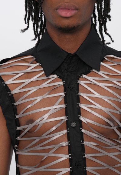 Chemise noire à manches courtes présentant un devant transparent avec des rubans argentés superposés en motif croisé, ornée de boutons le long de la patte.