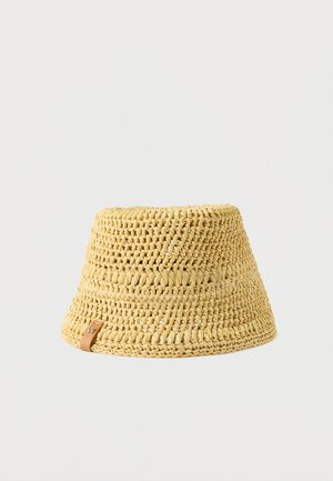 Chapeau cloche en crochet tissé jaune avec une petite étiquette en cuir beige sur le bord, présenté sur un fond blanc uni.