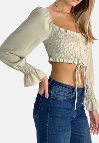 Beige kort topp med rynkad överdel, långa puffärmar och knytband vid midjan, kombinerad med högmidjade blå jeans.