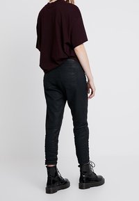 Musta nahkaverkkohousut, joissa on uritettu pinta ja kapenevat nilkat, yhdistettynä tummanpunaisiin löysiin t-paitoihin ja kiiltävään mustaan nauhattomaan saappaan.