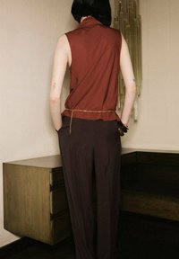 Top senza maniche bordeaux con un design drappeggiato, abbinato a pantaloni marroni a vita alta. Una sottile catena dorata valorizza la vita. Tessuto dalla consistenza liscia.