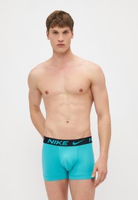 Nike muške bokserice u tirkiznoj boji s crnim pojasom na kojem se nalazi Nike logo. Materijal djeluje glatko, s pridržanom siluetom.