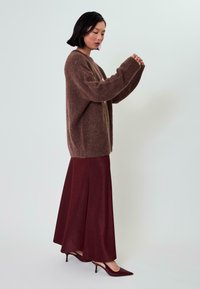 Rjav puhast oversized pulover, burgundska dolg plašč, ter čevlji s koničastim nosom. Mehki materiali z sproščenim oblikovanjem.