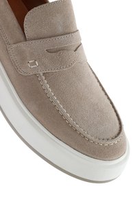 Beige suede slip-on shoe with a textured surface, white rubber sole, and decorative stitching along the edge. Classic loafer design.