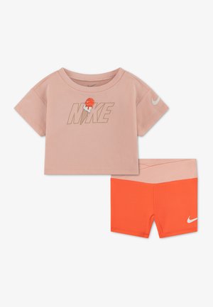 Jaunimo dviejų dalių komplektas: persikų spalvos trumpomis rankovėmis crop topas su Nike užrašu ir ledų grafika, derinamas su oranžinėmis šortais su rožine juosmens juosta.