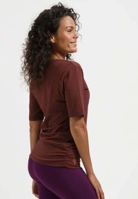 Bruin, kortermig T-shirt met een getailleerd ontwerp en zijdetails met plooitjes. Draagt bijpassende paarse legging. Gladde textuur, casual stijl.