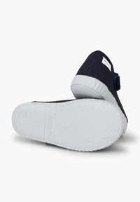 Zapatos de tela azul marino con suelas de goma blanca, que presentan una base texturizada y una correa de velcro para el cierre. Diseño sencillo sin patrón.
