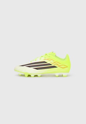 Scarpa da calcio di colore giallo neon con dettagli neri e arancioni, lacci e tacchetti modellati sulla suola, vista laterale.