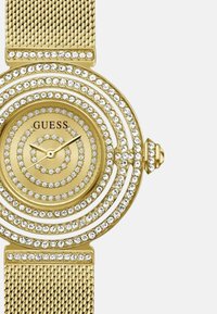 Zlatna narukvica sata od mrežice s okruglim licem, ukrašena s više redova umjetnih dijamanata i jednostavnim brojčaniku s imenom marke "Guess."