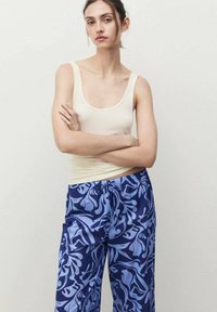 Romantop met brede bandjes in crème, gecombineerd met losse, gebloemde blauwe broeken met abstracte ontwerpen in marineblauw en lichtblauwe tinten.