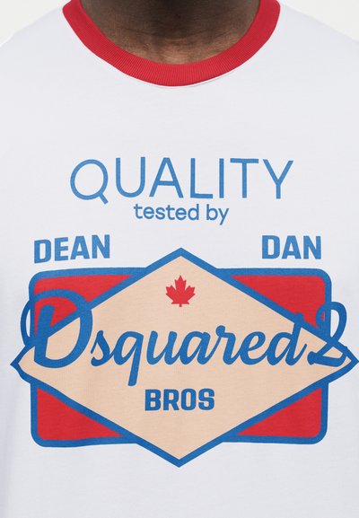 Λευκό T-shirt με κόκκινο γιακά που φέρει μπλε και κόκκινο γραφικό κείμενο: «QUALITY tested by DEAN DAN Dsquared2 BROS» και ένα μικρό κόκκινο φύλλο σφενδάμου.