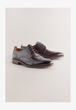 Pruunid nahast kleitjalatsid brogue-detailidega, lamedate nöörside ja terava varbaga, keskmise kannaga. Siledat tekstuuri täiendavad augujoonised.